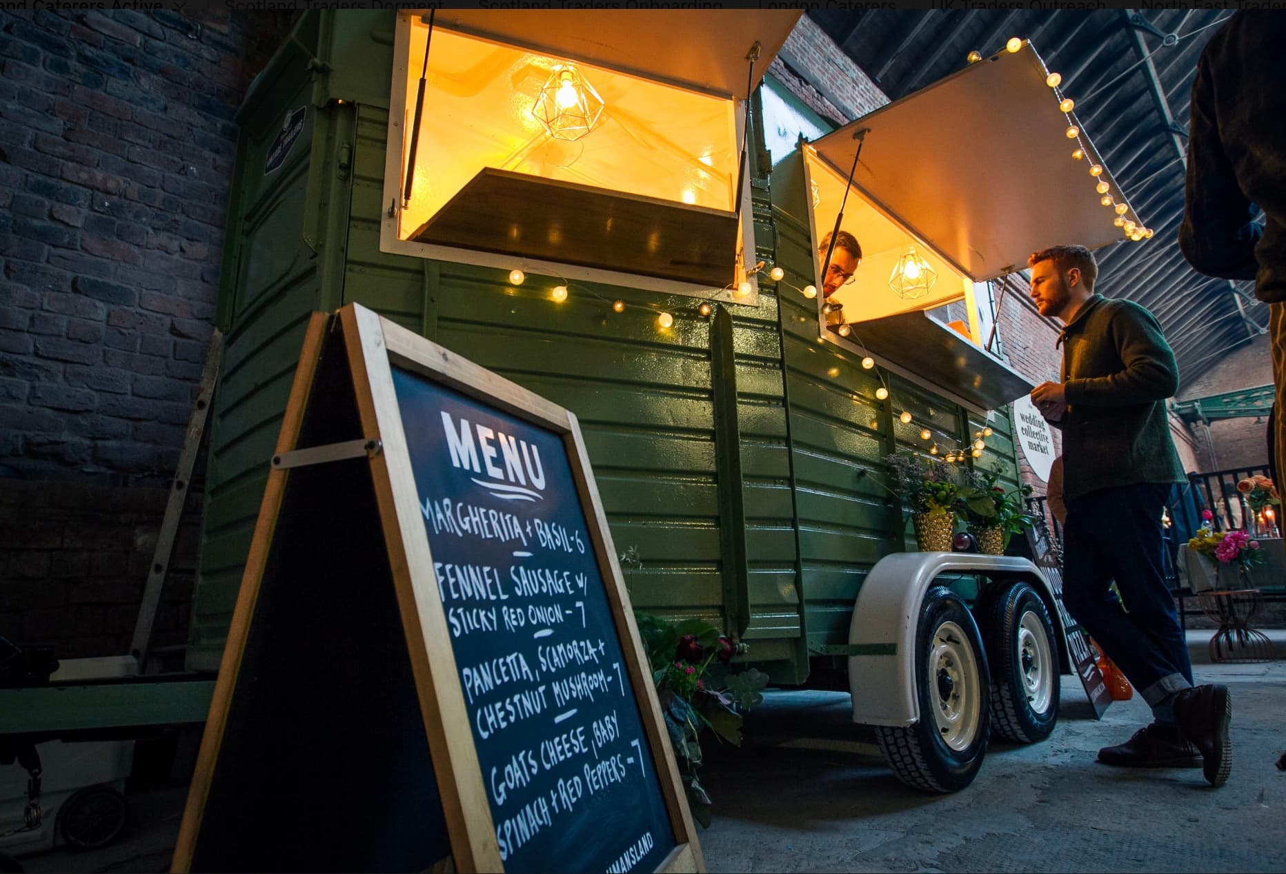 Green vintage food trailer with warm lights, a chalkboard menu, and a man standing outside.