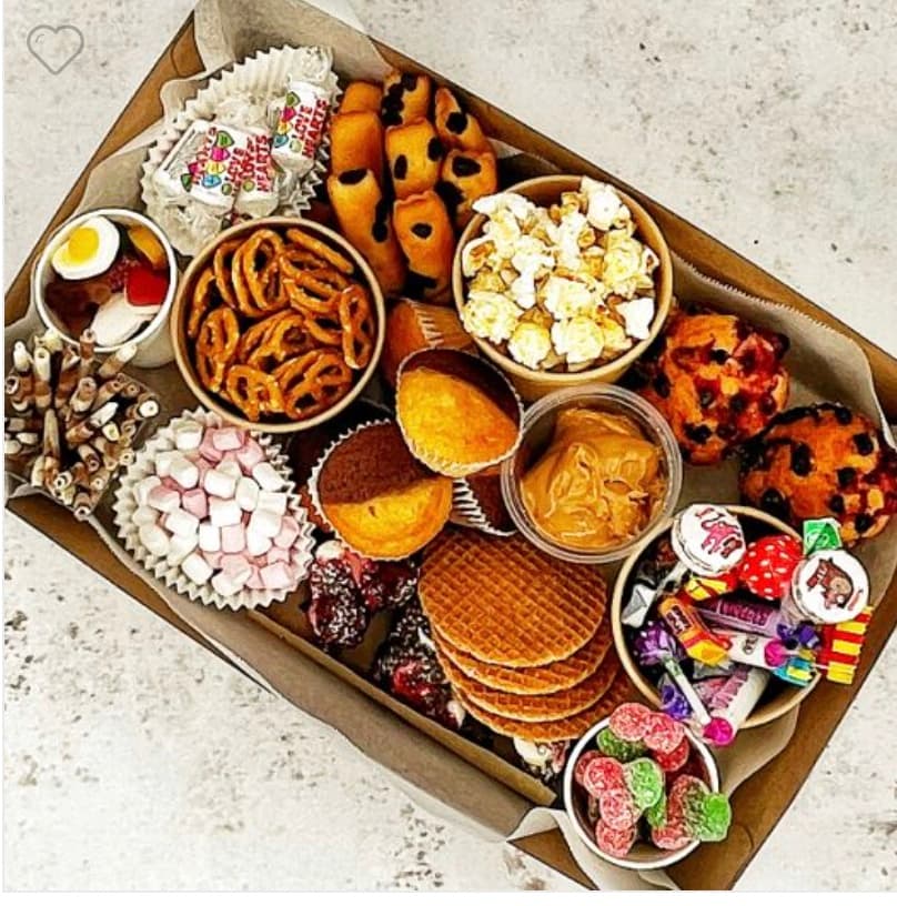 Cardboard box filled with assorted snacks including pretzels, popcorn, muffins, waffles, and colorful candies.
