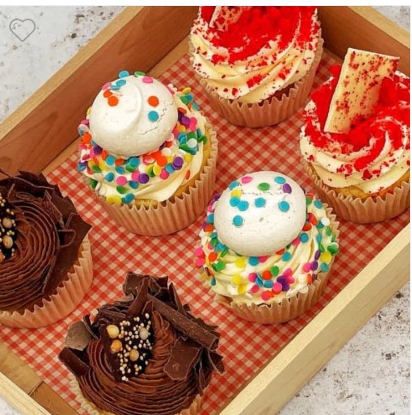 Six assorted cupcakes with chocolate, red velvet, and colorful sprinkle toppings in a wooden tray.