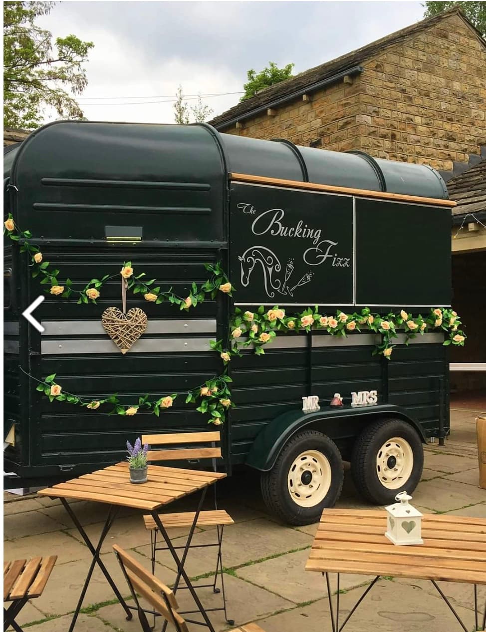 Dark green horse trailer mobile bar with floral garlands and "The Bucking Fizz" signage.